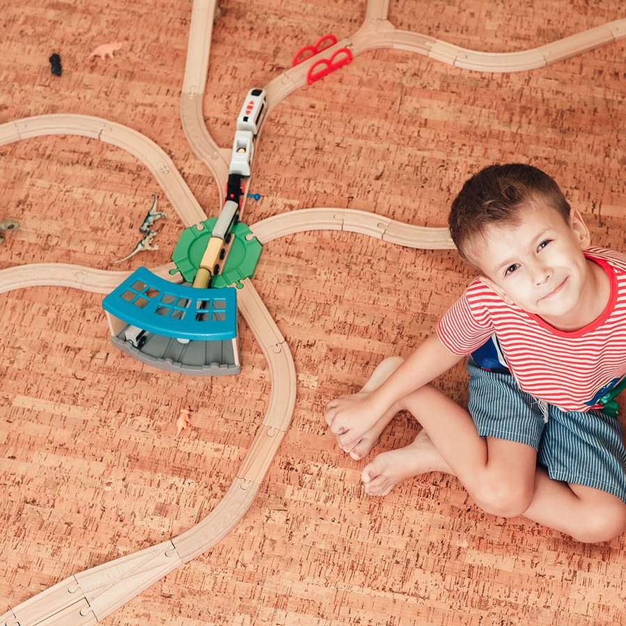 Junge spielt mit Holzeisenbahn auf Korkboden